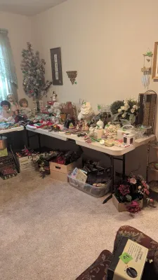 Sale Photo Thumbnail #39: Large collection of estate sale items including vintage dolls, ceramic figurines, holiday decor, artificial floral arrangements, and miscellaneous household goods displayed on folding tables.