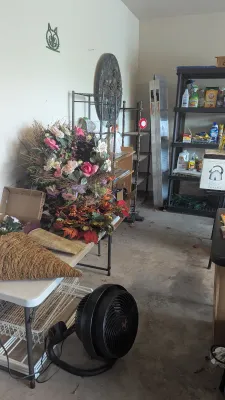 Sale Photo Thumbnail #32: Garage storage area featuring faux floral wreaths, a floor fan, shelving units, and various household supplies.