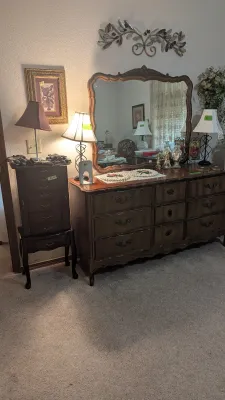 Sale Photo Thumbnail #20: French Provincial style dark wood dresser with matching mirror, flanked by a standing jewelry armoire, table lamps, and wall decor.