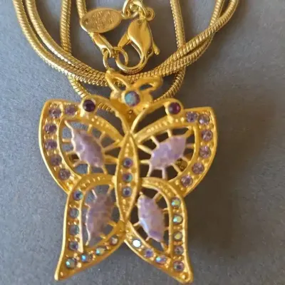Sale Photo Thumbnail #90: Gold-tone butterfly pendant necklace adorned with purple marquise stones and iridescent rhinestone accents, featuring a multi-strand snake chain and lobster claw clasp.