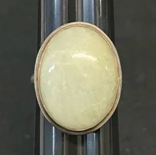 Sale Photo Thumbnail #13: Vintage sterling silver ring featuring a large oval pale green jade or quartz cabochon stone, shown on a ring sizer mandrel.