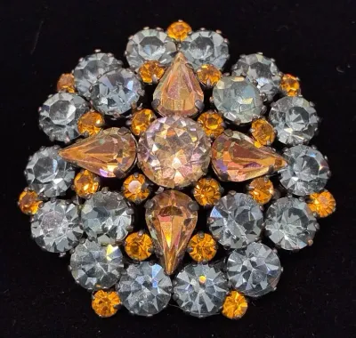 Sale Photo Thumbnail #84: Vintage dome-shaped rhinestone brooch featuring clear, amber, and pear-cut iridescent stones set in dark metal.