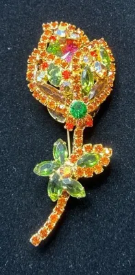 Sale Photo Thumbnail #113: Vintage gold-tone flower brooch featuring vibrant orange, green, and aurora borealis rhinestones in a stylized rose design.