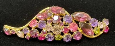 Sale Photo Thumbnail #117: Vintage gold-tone rhinestone brooch set with pink, purple, clear, and green faceted stones in a stylized leaf motif.