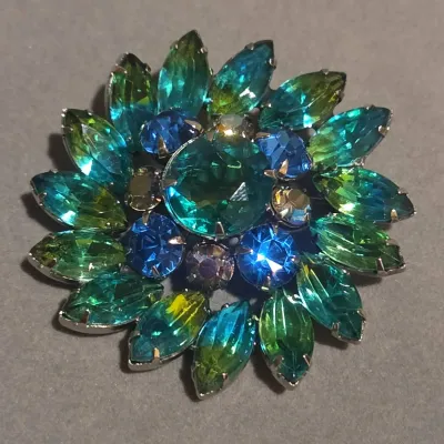 Sale Photo Thumbnail #35: Vintage flower brooch featuring prong-set green, teal, and blue rhinestones arranged in a layered starburst pattern.