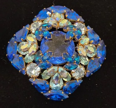Sale Photo Thumbnail #87: Vintage gold-tone rhinestone brooch featuring a central dark blue stone surrounded by tiered layers of cobalt blue and iridescent aurora borealis stones.