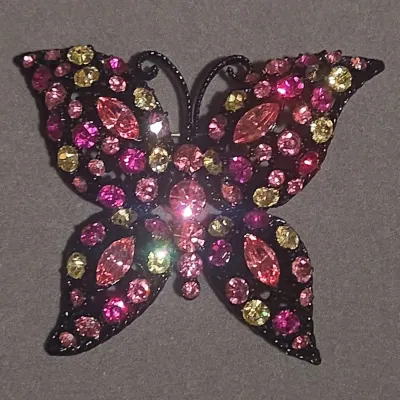 Sale Photo Thumbnail #38: Butterfly-shaped costume jewelry brooch set with pink, magenta, and yellow rhinestones on a dark metal frame.