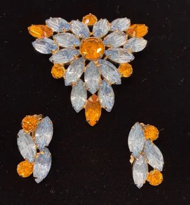 Sale Photo Thumbnail #72: Vintage mid-century rhinestone jewelry set featuring a triangular brooch and matching clip-on earrings with light blue marquise-cut and amber-colored round stones.