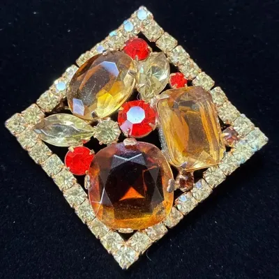 Sale Photo Thumbnail #57: Vintage diamond-shaped costume jewelry brooch featuring large topaz, amber, and red rhinestone accents set in a pave-style frame.