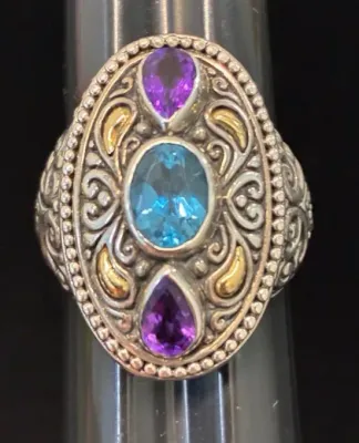 Sale Photo Thumbnail #116: Ornate silver and gold-tone statement ring set with a central oval blue topaz and two teardrop amethyst gemstones.