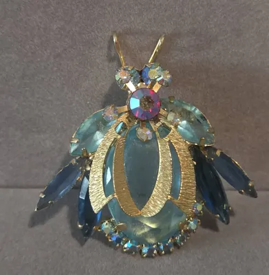Sale Photo Thumbnail #24: Vintage insect or beetle brooch featuring light and dark blue rhinestone accents and textured gold-tone details.