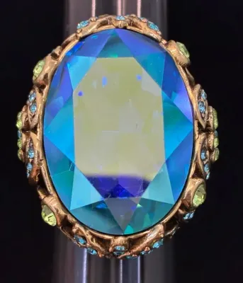 Sale Photo Thumbnail #100: Vintage gold-tone cocktail ring featuring a large oval iridized blue glass center stone accented by small blue and light green rhinestones.