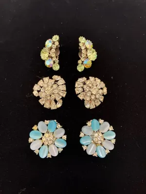 Sale Photo Thumbnail #47: Collection of three pairs of vintage clip-on earrings, featuring aurora borealis rhinestones, clear cut-glass clusters, and blue and white cabochon flower motifs.