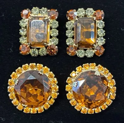 Sale Photo Thumbnail #66: Two pairs of vintage clip-on costume earrings featuring large amber-colored rhinestones surrounded by smaller coordinating crystals, set in gold-tone metal.