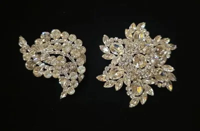 Sale Photo Thumbnail #37: Pair of vintage clear rhinestone brooches, including a curved swirl motif and a starburst design, set on silver-tone metal backing.
