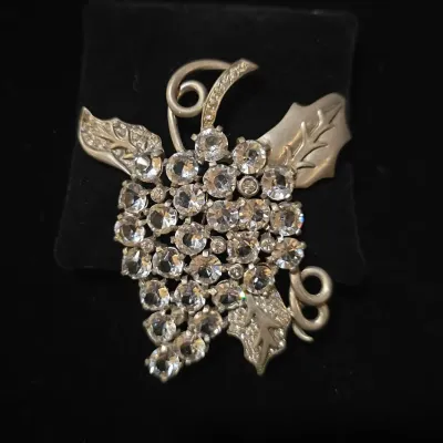 Sale Photo Thumbnail #31: Vintage grape cluster brooch featuring clear faceted rhinestones and silver-tone leaves and tendrils.