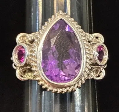 Sale Photo Thumbnail #108: Sterling silver cocktail ring featuring a large teardrop-cut purple amethyst center stone flanked by two round magenta accent stones with rope-edge detailing.