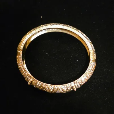 Sale Photo Thumbnail #45: Ornate gold-tone hinged bangle bracelet set with clear rhinestone pavé and small pearl accents, displayed on a black fabric background.