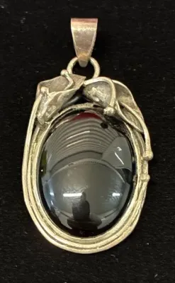 Sale Photo Thumbnail #4: Vintage sterling silver oval pendant featuring a polished black onyx or hematite cabochon framed by a floral calla lily design.