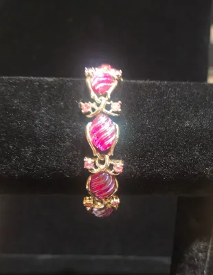 Sale Photo Thumbnail #40: Vintage gold-tone costume jewelry bracelet featuring swirled fuchsia glass cabochons and light pink rhinestone accents displayed on a black velvet stand.