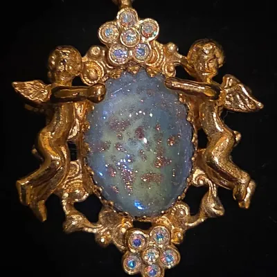 Sale Photo Thumbnail #25: Vintage gold-tone cherub pendant brooch featuring a central iridescent faux opal cabochon flanked by winged angels and iridescent rhinestone clusters.