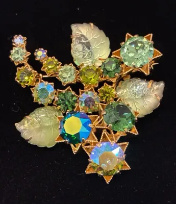 Sale Photo Thumbnail #75: Vintage gold-tone floral brooch set with green rhinestones, iridescent aurora borealis crystals, and carved glass leaves.