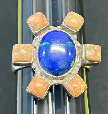 Sale Photo Thumbnail #105: Southwestern-style sterling silver statement ring featuring a central oval lapis lazuli cabochon surrounded by six square orange spiny oyster shell accents.