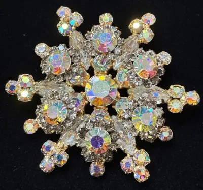 Sale Photo Thumbnail #61: Vintage snowflake-style brooch set with iridescent aurora borealis rhinestones in a gold-tone prong setting.