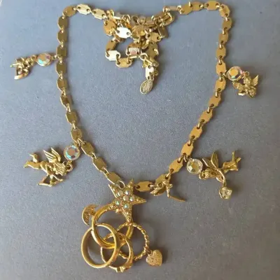 Sale Photo Thumbnail #65: Vintage gold-tone charm necklace featuring cherubs, rhinestone accents, and intertwined ring motifs.