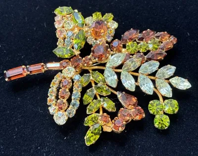 Sale Photo Thumbnail #71: Vintage autumn-toned rhinestone leaf brooch set in gold-tone metal, featuring peridot, amber, and light blue crystals in a floral spray design.