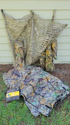 Assortment of camouflage hunting gear, including a ground blind with netting, camo tarps, and packaged camo material.