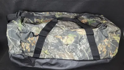 RedHead camouflage duffel bag featuring double carry handles, a black shoulder strap, and a reinforced vinyl bottom.