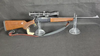 Browning BLR lever-action rifle featuring a gloss wood stock with checkered grip, mounted scope, attached sling, and gold-colored trigger.