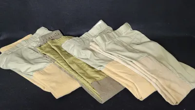 Folded group of men's vintage hunting and utility pants in khaki and olive tones, featuring reinforced leg panels.