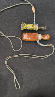 Two wooden game calls attached to a lanyard, including a Primos Old Crow call and a polished wood waterfowl call.