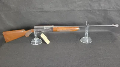 Vintage Browning Auto-5 semi-automatic shotgun with an engraved receiver and checkered walnut stock, displayed on clear acrylic stands.