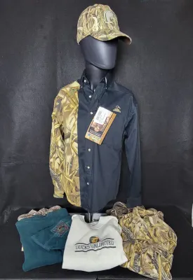 Ducks Unlimited apparel collection featuring a split-design button-down shirt with retail tags, a camouflage cap, and folded shirts and...