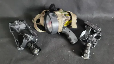 Collection of portable lighting gear, including two modern LED headlamps and a Vector camouflage hand-held spotlight with a shoulder strap.