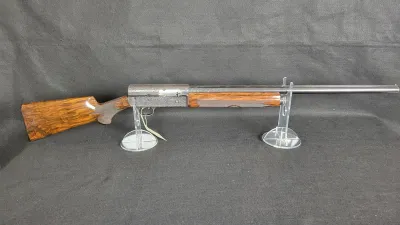 Browning Auto-5 semi-automatic shotgun with a checkered figured walnut stock and an engraved receiver, displayed on clear acrylic stands.