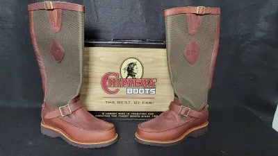 Pair of tall Chippewa brown leather and canvas snake/hunting boots with buckle straps, displayed in front of their original box.