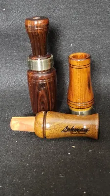 Set of three vintage wooden game calls, including one stamped with the Lohman brand name, featuring brass accents and smooth glossy...