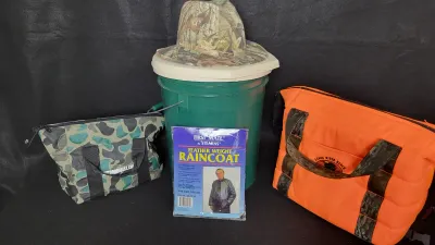 Collection of outdoor gear including a blaze orange tote bag, camouflage lunch bag, green plastic bucket with a camouflage brimmed hat,...