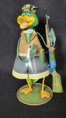 Whimsical painted metal duck hunter figurine, featuring camouflage hat, rifle, shotgun shells, and webbed feet on a round base.