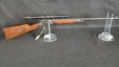 Vintage lever-action rifle featuring a wooden stock and an attached telescopic sight, displayed on clear acrylic stands.