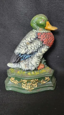 Vintage painted cast iron duck doorstop featuring a detailed mallard figure mounted on a decorative green and gold base.