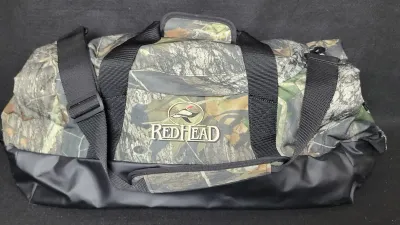 RedHead brand camouflage duffel bag featuring a durable black vinyl base, adjustable shoulder strap, and double carrying handles.