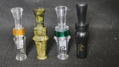 Collection of four Ducks Unlimited duck calls, including acrylic and resin designs in clear, green swirl, and matte black.