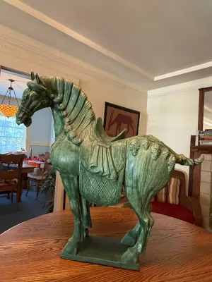 Sale Photo Thumbnail #184: Large Tang Dynasty-style green glazed ceramic horse statue with detailed saddle and bridle, displayed on a wooden table.