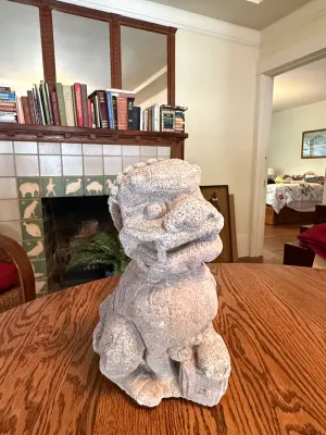 Sale Photo Thumbnail #175: Hand-carved stone Asian Foo Dog statue resting on a wooden tabletop.