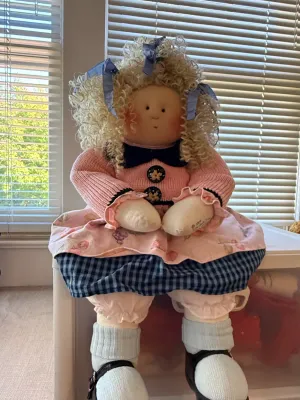 Sale Photo Thumbnail #355: Handmade soft rag doll featuring curly blonde hair with blue ribbons, a pink knit sweater, patterned dress, and white socks with shoes.